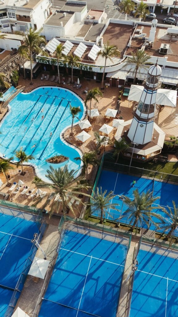 Aerial view of Hotel Fariones Lanzarote outdoor pool, paddle tennis courts and palm trees in Puerto