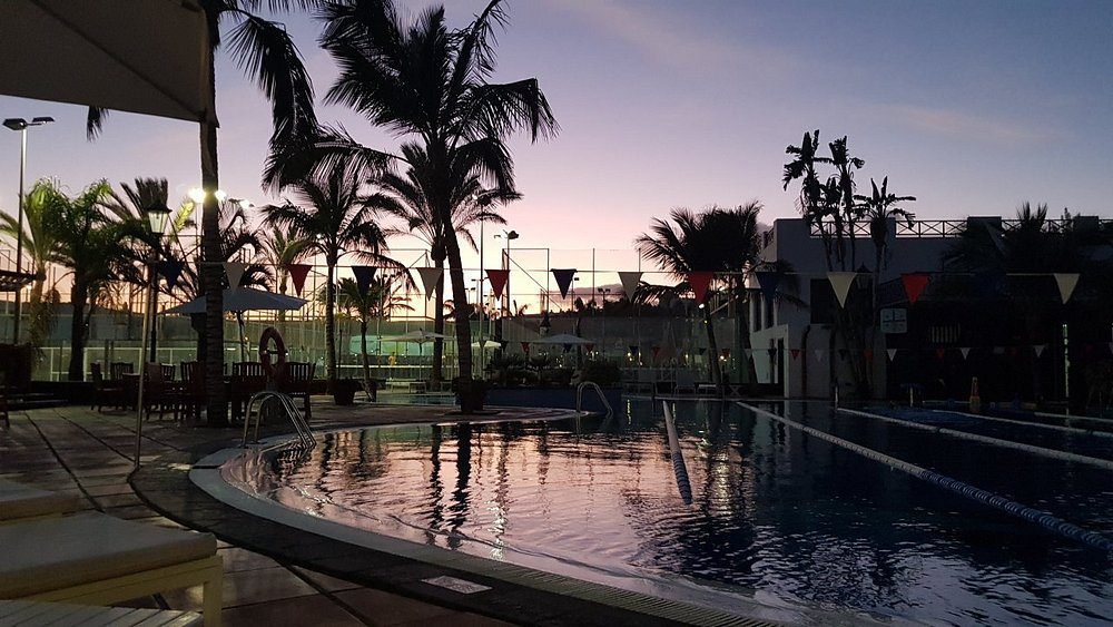Outdoor pool at dusk with palm trees and sports courts at luxury Hotel Fariones Lanzarote Puerto del