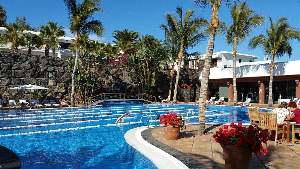 Outdoor swimming pool surrounded by palm trees and red flowers at luxury Hotel Fariones Lanzarote